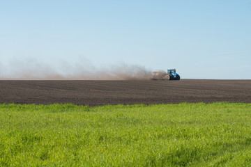 blue tractor plowing field with electric power transmission pylons on background
