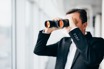 american businessman using binoculars look in windows in office