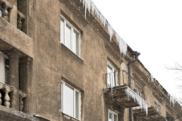 Fototapeta na wymiar Dangerous long icicles hanging on the roof and balcony of the old building in winter