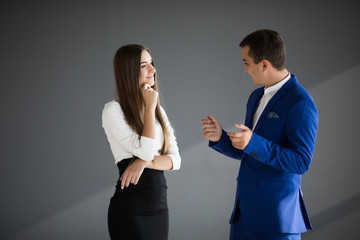 Serios businesswoman and businessman are conversing against grey background.