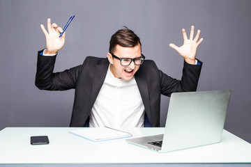 Angry senior businessman sitting at his desk and screaming. Angry businessman with too much work in office. Handsome stressed young man in glasses using laptop