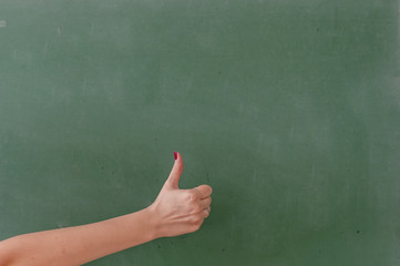 Like this. Close-up of human hand with thumb up in front of the blackboard