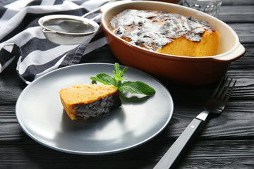 Plate and baking dish with tasty carrot souffle on wooden table