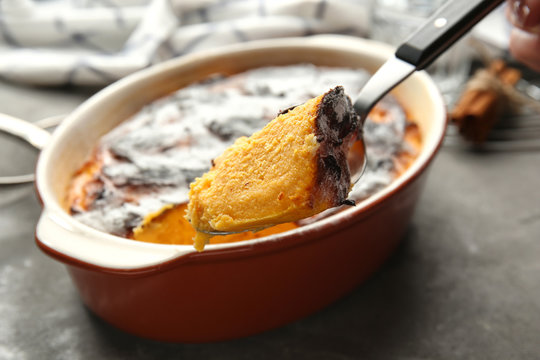 Spoon with tasty carrot souffle and baking dish on table