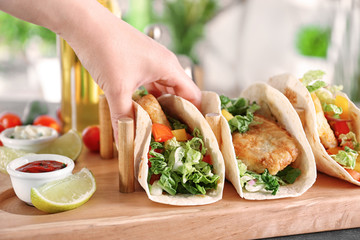 Woman holding delicious fish taco in kitchen
