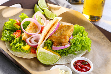 Wooden tray with delicious fish tacos on kitchen table