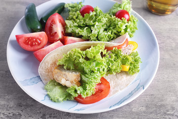 Plate with delicious fish taco and vegetables on kitchen table