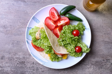 Plate with delicious fish taco and vegetables on kitchen table