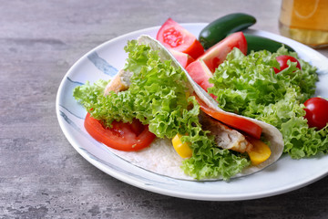 Plate with delicious fish taco and vegetables on kitchen table