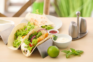 Holder with delicious fish tacos on wooden table