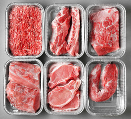 Containers with pieces of different fresh meat on grey background