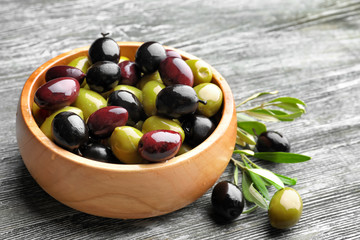 Bowl with different olives on wooden background