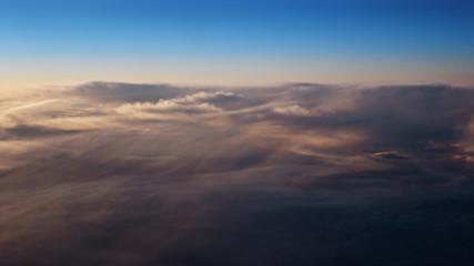 Flying over the evening clouds with the late sun. Flight through moving cloudscape with beautiful sun rays. Traveling by air through an airplane window. Perfect for posters, background