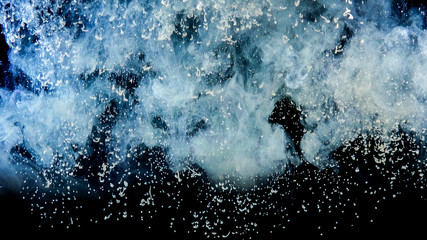 White paint drops from above mixing in water. Ink swirling underwater. Cloud of ink isolated on black background. Abstract smoke explosion effect with particles. Close up view