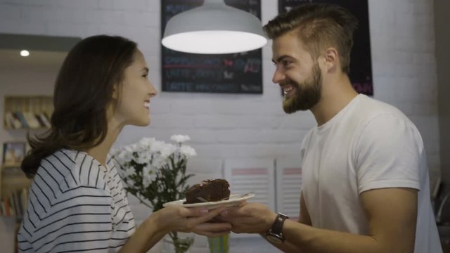 Young handsome bartender giving cake to smiling beautiful female customer