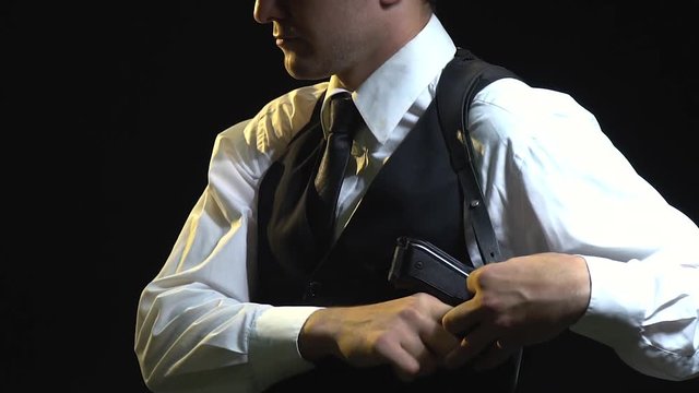 The detective in a black hat pushes the gun into his holster and looks into the camera, slow motion