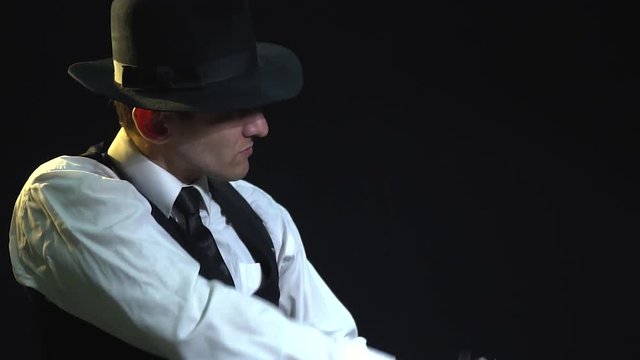 A detective in a suit and hat takes out a pistol from his holster and aims to the side