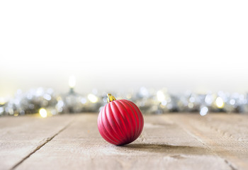 Red Christmas ornament sitting on rustic wooden table or floor, tinsel with light