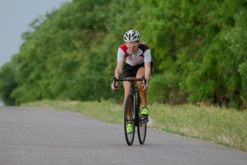 Fototapeta premium Bicycle racer in helmet and sportswear training alone on empty country road, fields and trees background 