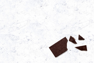 Broken dark chocolate bar isolated on a white marble kitchen top. Horizontal composition. Top view
