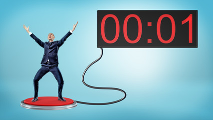 A victorious businessman on a large red push button connected to a screen with one remaining second.