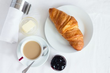 Top down view of croissant served with coffee, butter and blueberry jam