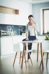 Young woman with orange juice and tablet in kitchen.