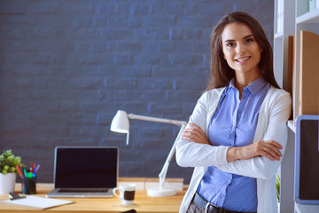 Young woman standing near desk with laptop