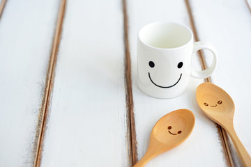 Happy cup and smiley wooden spoons with happiness on wooden texture of dining table. Concept about love and relationship. Friendship and teamwork idea.