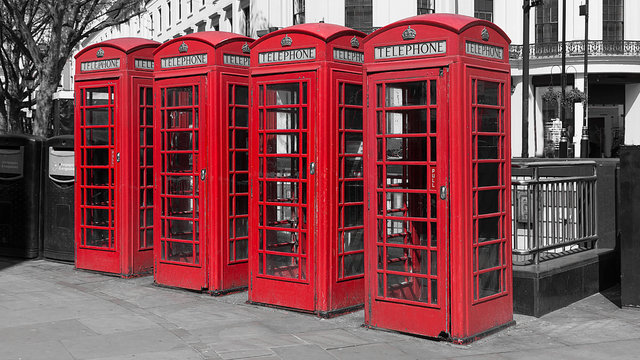 Black and white image with four colour color popped red uk telephone boxes in a line in a london street