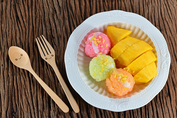 Top view of fresh mango and colorful sticky rice on white plate with smiley wooden spoon. Thai famous fruits. Concept about love and relationship with happiness. Homemade dessert.