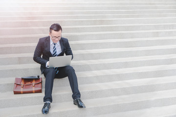 Asian Smart Businessman working with laptop and sitting on stairs.Concept of success business.