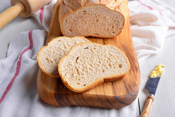 Sliced French bread on cutting board with knife spreading butter on white wooden table. Homemade bakery concept. Food preparation for family. Morning breakfast with healthy and clean foods