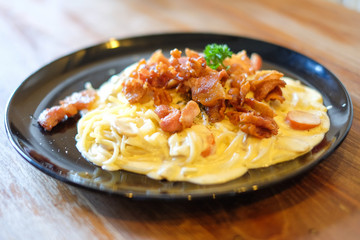 The spaghetti carbonara with bacon and mushroom cream sauce on black dish set on brown wooden table for food background or texture - homemade food concept.