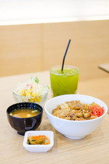 The food set consists of rice with grilled pork teriyaki, spring onion & carrot on top white bowl serve with tofu soup (Miso soup), tomato, cabbage & corn salad and green tea - japanese food concept.