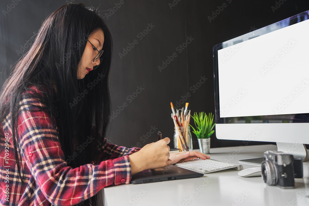 Fototapete Young asian female designer using graphics tablet while working with computer at studio or office.