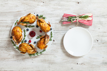 Festive table on christmas holidays. Table appointments waiting for guests. Baked quails on white plate. White plate, spoon and fork on wooden table. Top view. Happy New Year concept.