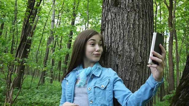 Girl taking selfie photo smartphone at park in summer. Posing and smiling. Video footage.