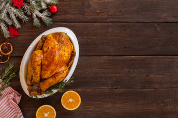 Baked chicken on white plate. Christmas dish on a dark wooden background. Top view. Copy space. Winter holidays concept. Culinary background for recipe of christmas dishes.