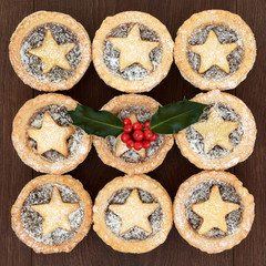 Home made christmas mince pies with pastry stars and icing sugar dusting, holly and red berries on oak wood background.