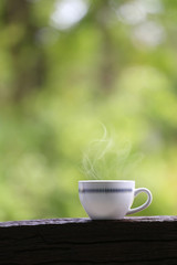 White coffee mug on wooden floor and green nature background.