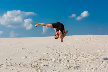 Portrait of young parkour man doing flip or somersault on the sand.
