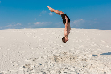 Portrait of young parkour man doing flip or somersault on the sand.