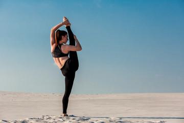 Young slim woman do gymnastic exercise at white sand beach under blue sky.