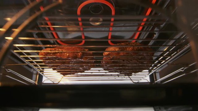 Broiling beef marbled steaks in the oven with broiler. Grill element glowing red. Juicy grilled ribeye steaks on grilling rack under high heat. Meat juices dripping onto a drip pan.