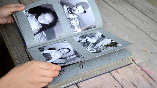 Girl leafing through a photo album with old photos which lies on the table close-up