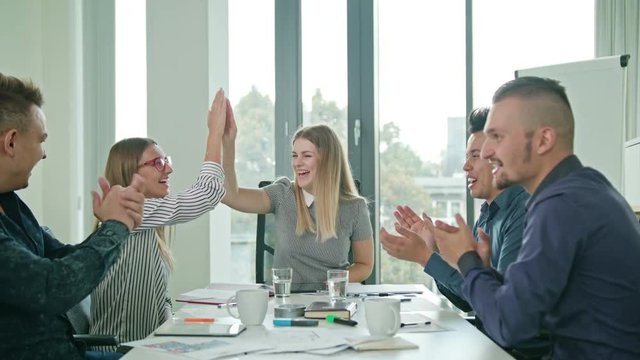 Diverse group of creative business team members with female team leader celebrating with high fives at a startup in a modern office in slow motion