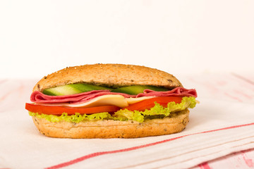 Sandwich with cheese, tomato, salami, cucumber and lettuce on wooden table