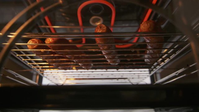 Broiling beef sausages in the oven with broiler. Grilling rack with browned sausages under high heat. Grill element glowing red. Meat juices dripping onto a drip pan. View from inside of electric oven