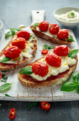 Tomato Ricotta Bruschetta with sun dried tomatoes paste, olive oil brown bread and basil in a white wooden board.